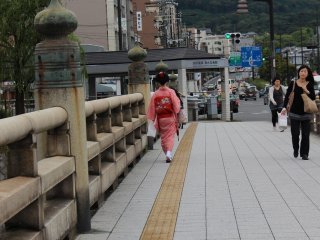 Here, a traditional entertainer known as a Maiko can be seen crossing the Gojo Oohashi Bridge, which extends over the secondary branch of the Kamogawa River