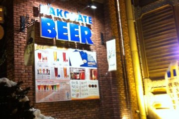 <p>ด้านหน้าของร้าน Hakodate Beer Hall ยามค่ำคืนที่หิมะโปรยปราย</p>