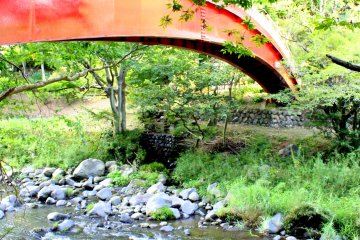 <p>The red bridge over the shallow rushing waters gives a perfect contrast to the green surroundings</p>