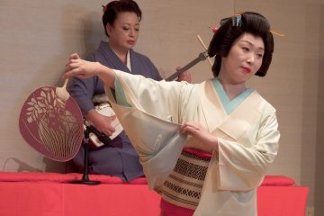 <p>Ms. Shiori,&nbsp;summer fan in her hand, is posing in motion. Ms. Madoka is playing Shamisen in the background</p>