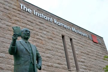 <p>Mr. Momofuku Ando standing with pride at the entrance of The Momofuku Ando Instant Ramen Museum</p>