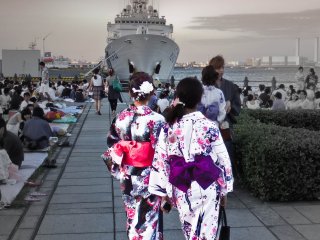 A couple of young women wait patiently for the display to begin near the &#39;Aka-Renga&#39; area. Note the large ship in the background that belongs to the Japanese Coast Guard, which maintains a small patrol base here
