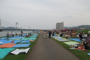 People lay out tarps on the riverside to sit on during the fireworks display