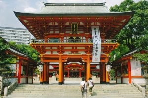 Sebuah gerbang utama dari kuil Ikuta. Terlihat bangunan ini memiliki banyak ornamen dan dipenuhi warna merah. Ini merupakan salah satu simbol Kuil Shinto.