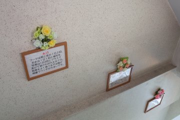 <p>Even these information plaques in the stairwell have a cute, homely d&eacute;cor, adorned in plastic flowers</p>