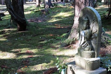 <p>Statue Number six sits silently on the ground on which some brown leaves have fallen</p>