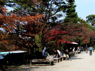Tourists rest on benches along the path opposite the castle