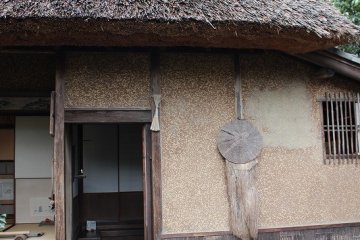The outside of the "Hut of Fallen Persimmons". During the Edo period, the straw coat and hat hanging on the wall would have indicated whether the residents were home.