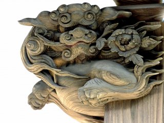 A carved shishi holding a peony stem in its mouth