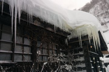 <p>Icicles hang from the eaves of snow-covered roofs</p>