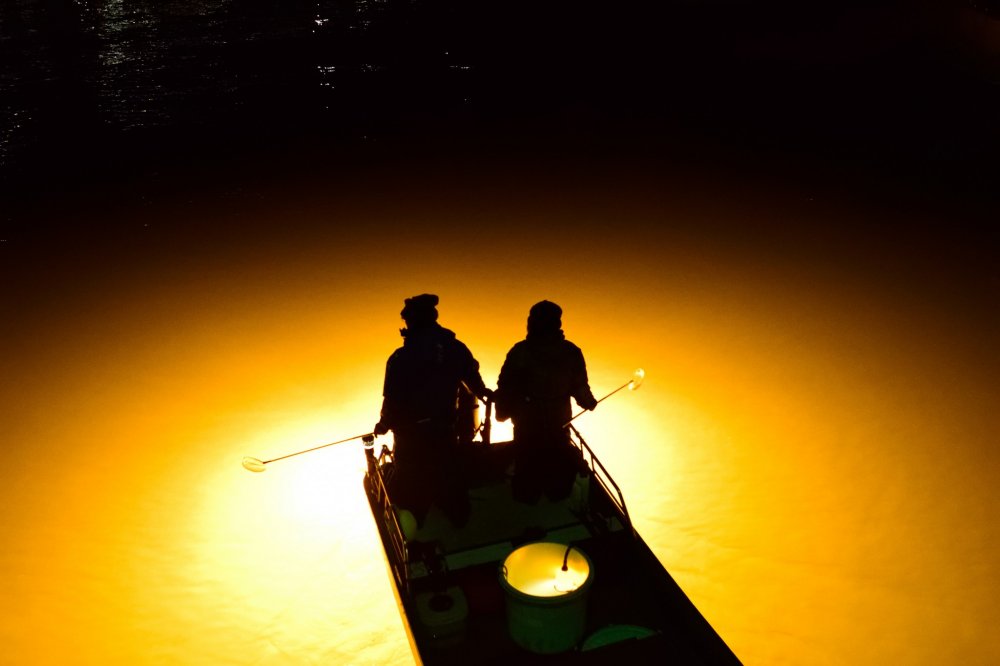 川面に広がった光芒が、漁師のシルエットを浮かび上がらせる（新町川）