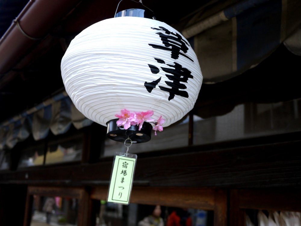 Lồng đèn giấy được trang trí với hoa anh đào và nhân vật Kusatsu treo tại mái hiên của mọi cửa hàng