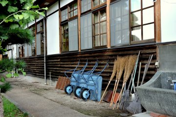 Wheelbarrows and brooms lean against a building's side