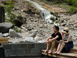 Des visiteurs sont assis au bord d'un bassin, devant une cascade d'eau chaude