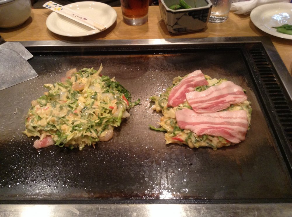 Okonomiyaki babi dan campuran (makanan laut dan rasa daging) dipanggang di atas wajan panas