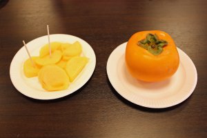 Sliced kaki (Japanese persimmon) next to the real thing. Despite its resemblance to an orange tomato, the kaki have a texture like an apple and taste like something between an apple and a pear.