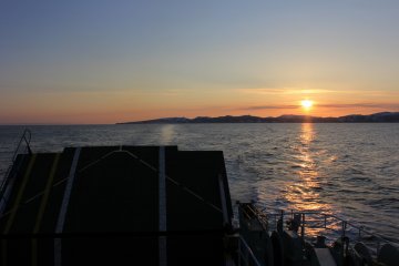 The ferry gets further away as the sun sets.