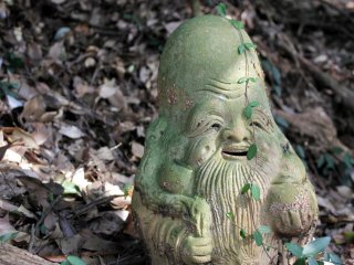 Pho tượng một ông lão đầu to đứng đơn độc trong khu rừng phía sau đền 