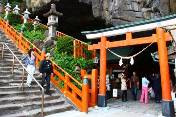 Make your way carefully down a flight of stone steps to the shrine entrance, marked by a red torii in the mouth of the cave.