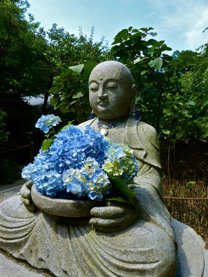 <p>Jizo statue holding blue hydrangea flowers</p>