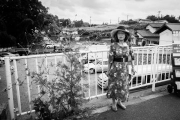 Here's a B&W photo of a somber Japanese lady waiting for her travel group on the side of a bridge at red spider lily festival in Saitama.