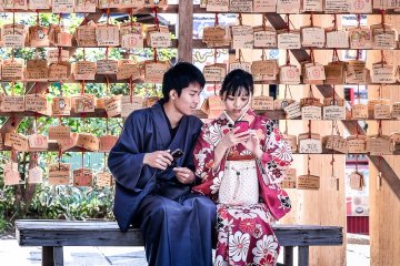 A couple wearing kimono in front of prayer tablets