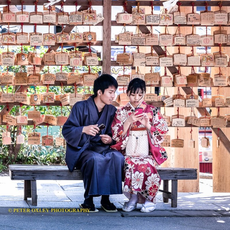 A couple wearing kimono in front of prayer tablets